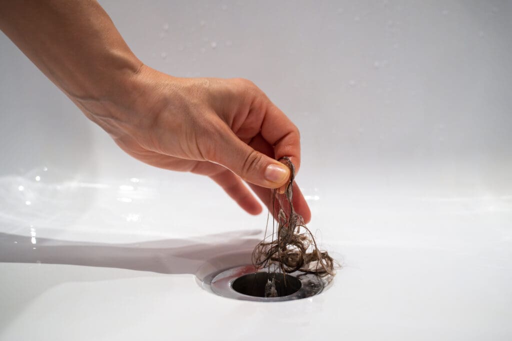 A hand pulls a tangled clump of hair out of a white sink drain.