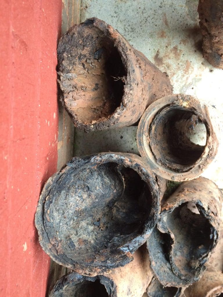 Several heavily corroded and rusted metal pipes are stacked on a surface next to a red wall, showing severe internal decay and flaky, rough textures.